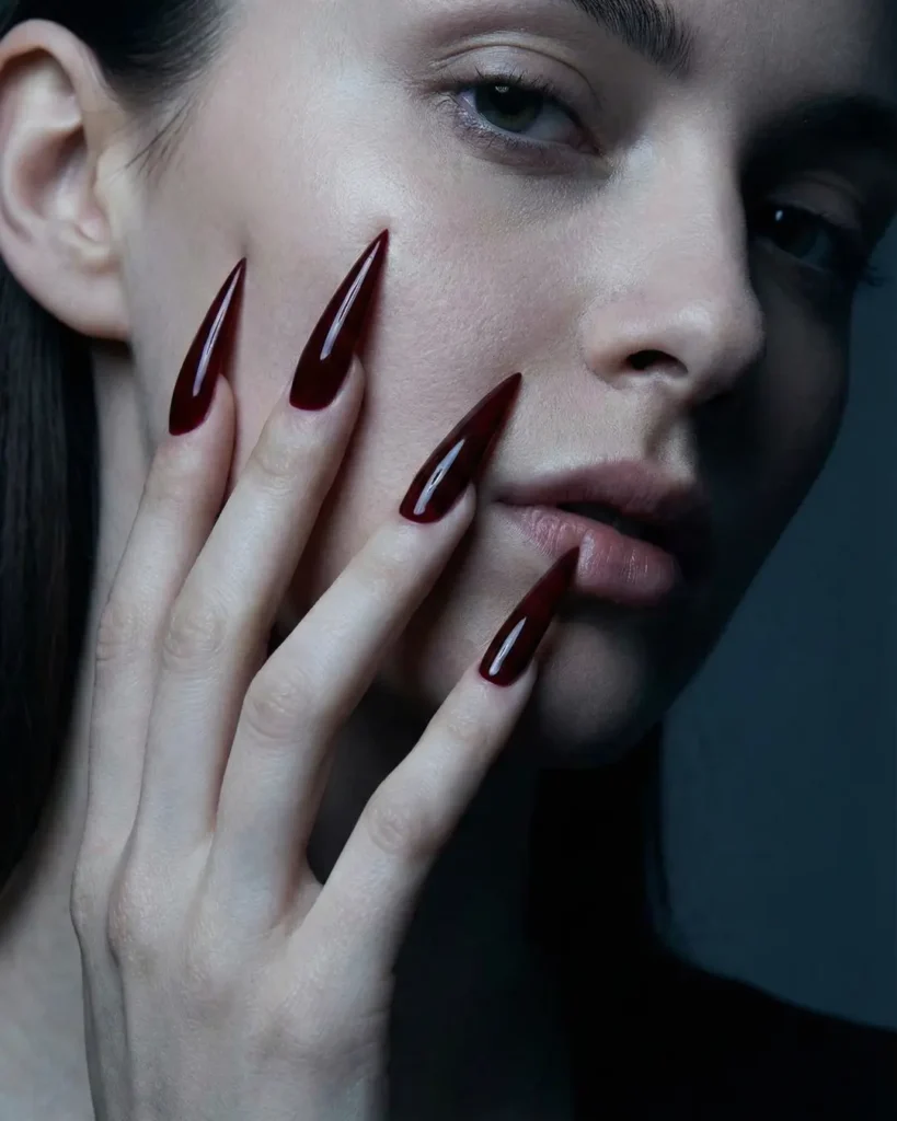 Extra long sharp stiletto nails in vampy red, filed to a needle point for a dramatic look.